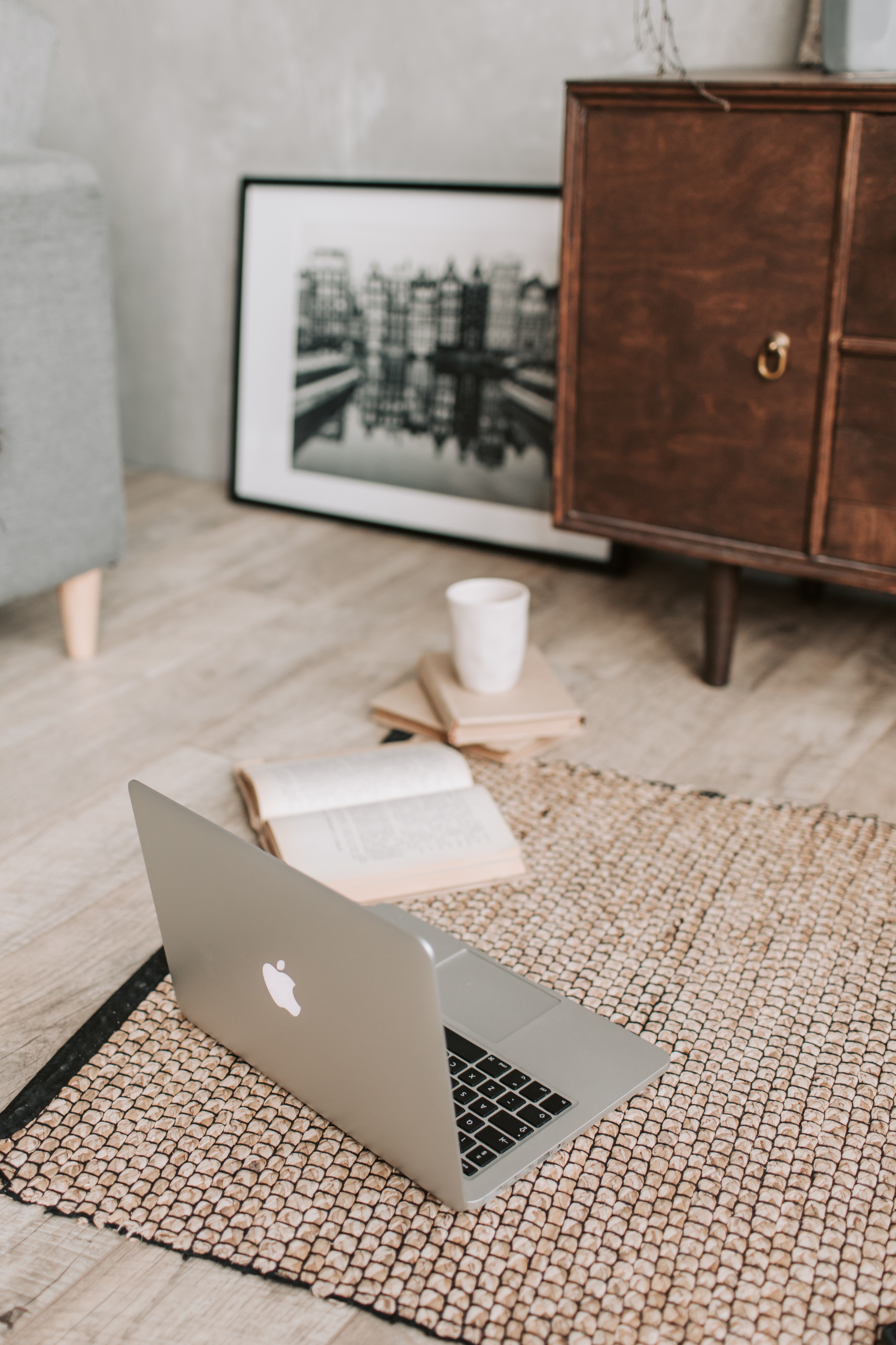 Stock photo showing macbook laptop, coffee, book, on area rug surrounded by furniture.